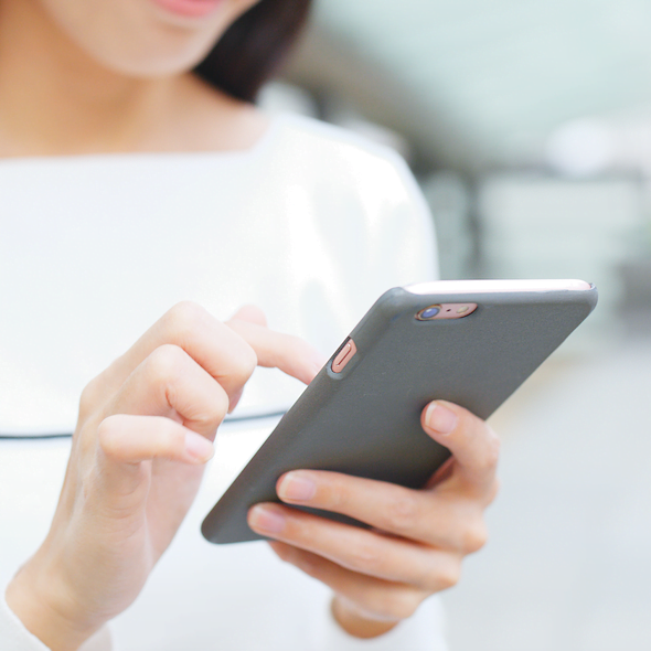 Close up of a woman in a white blouse typing and scrolling on her mobile phone with a grey cover.