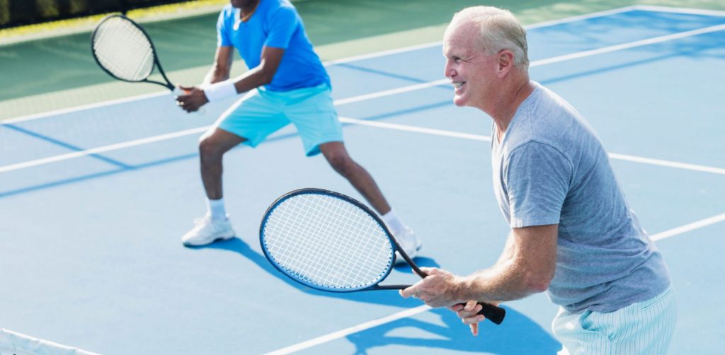 Older gentleman plays tennis while smiling.