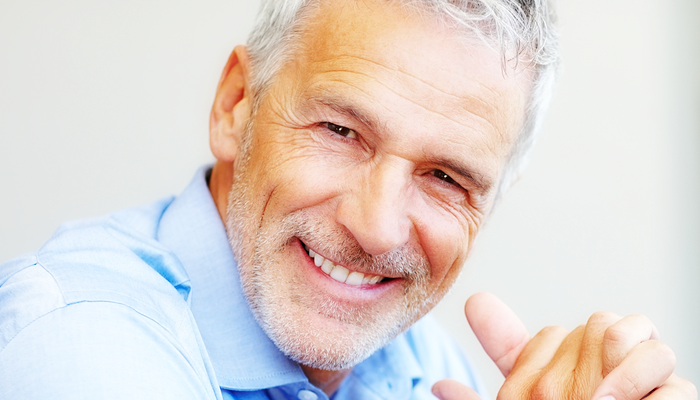 Close up of older man in blue shirt smiling for the camera.